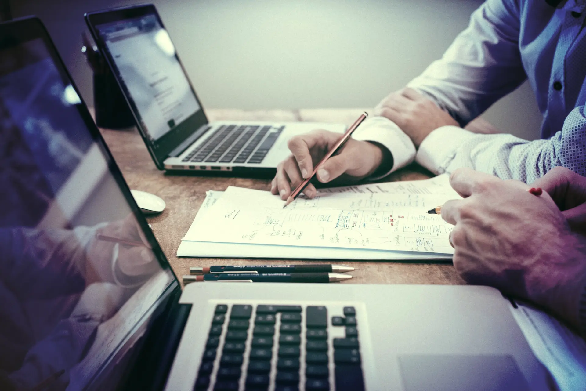 person holding pencil near laptop computer